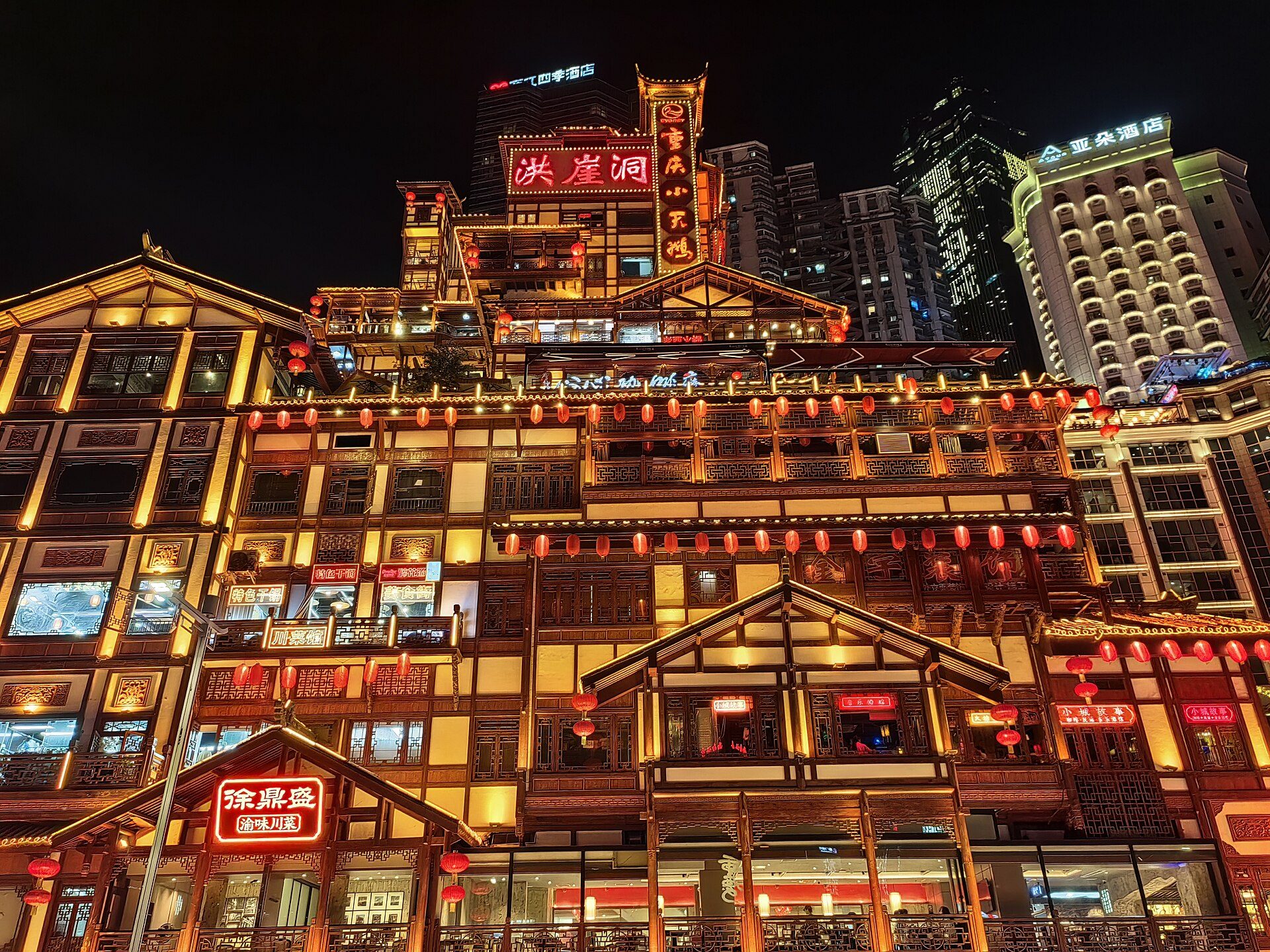 Hongyadong glowing at night in Chongqing with red lanterns, illuminated facades, and high-rises behind it.