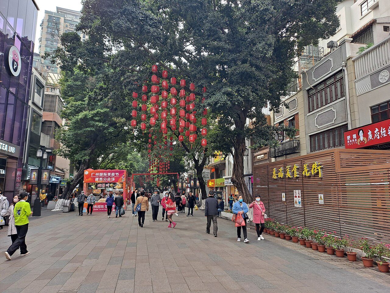 Pedestrians walking along Beijing Road in Guangzhou beneath lanterns and large shade trees.