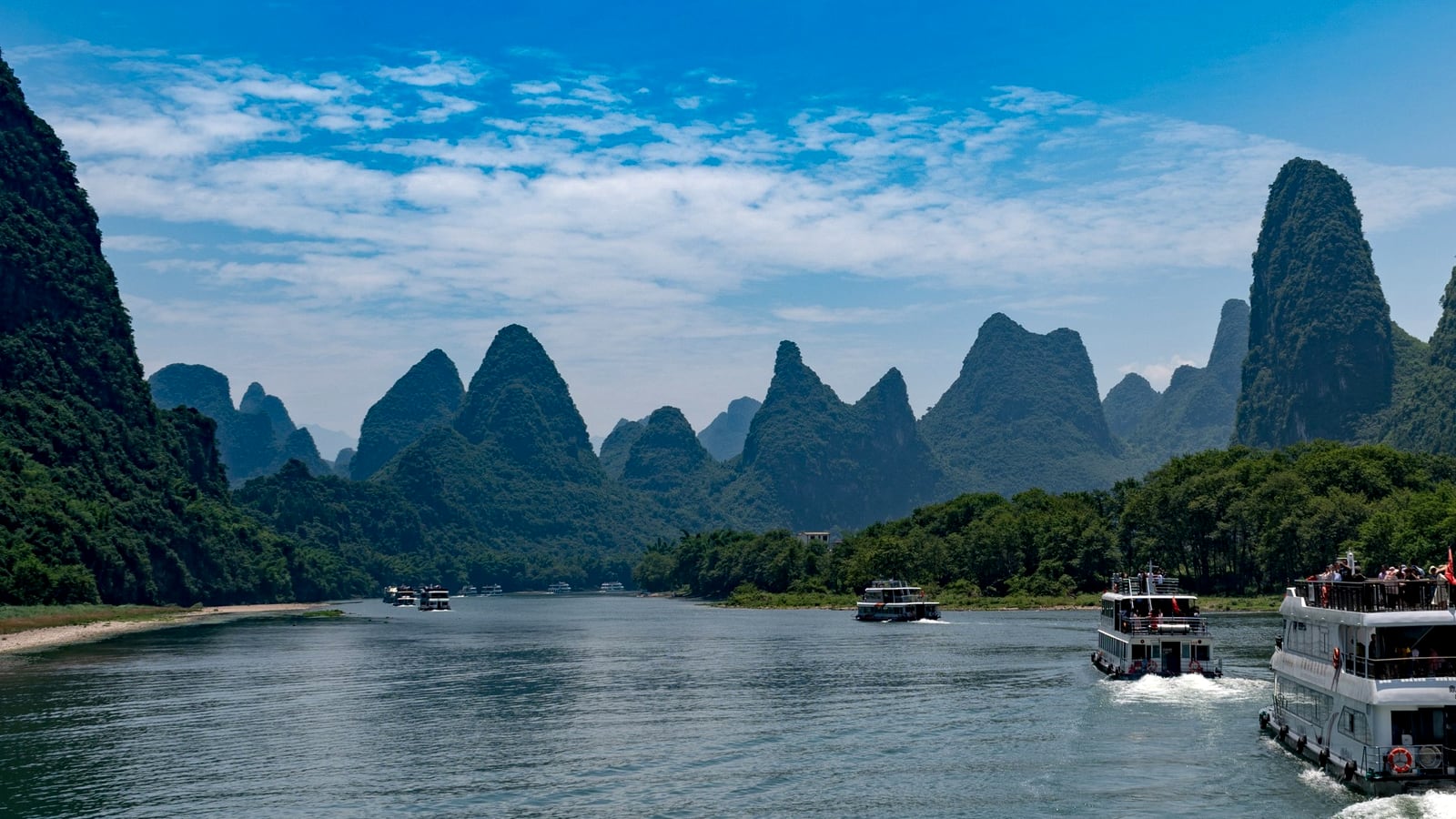 Cruise boats on the Li River in Guilin framed by classic karst peaks under a bright blue sky.