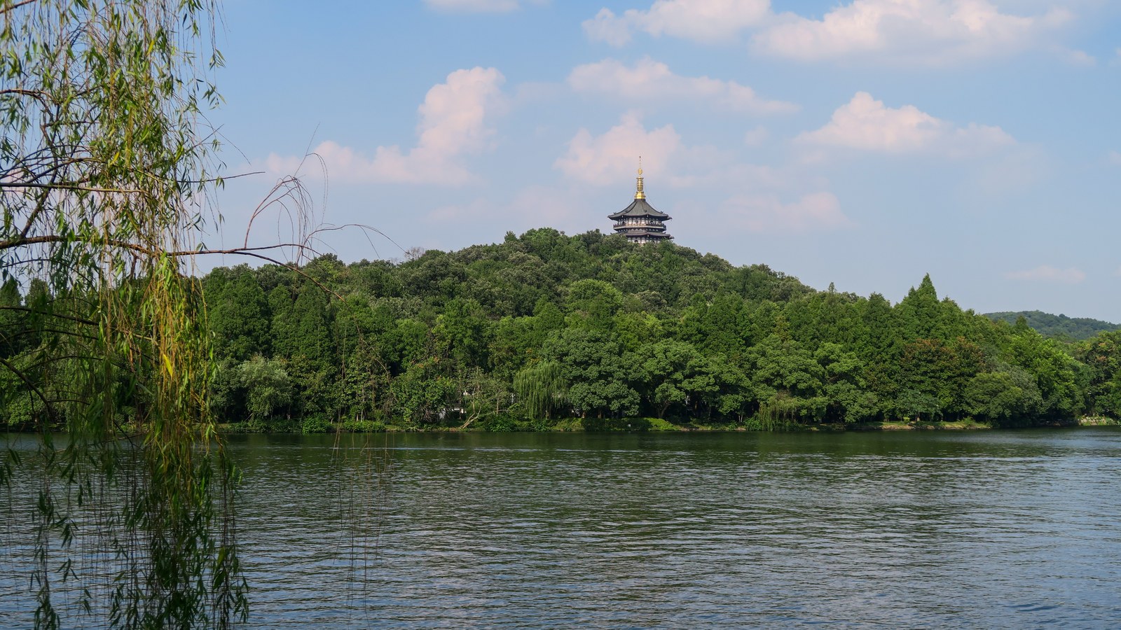 Leifeng Pagoda rising above the trees across West Lake in Hangzhou with willow branches framing the water.