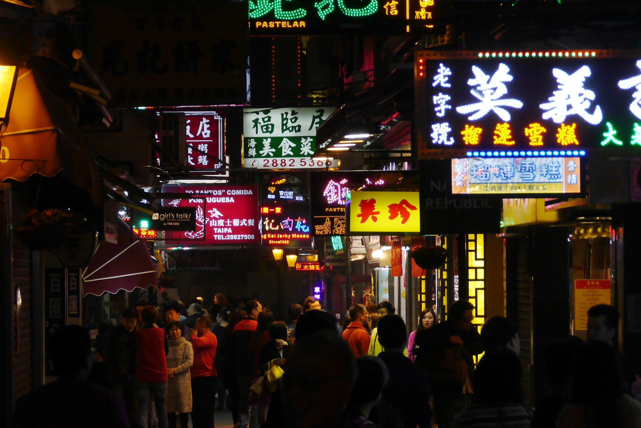 A busy Taipa Village street in Macau glowing with shop signs and evening food-street energy.