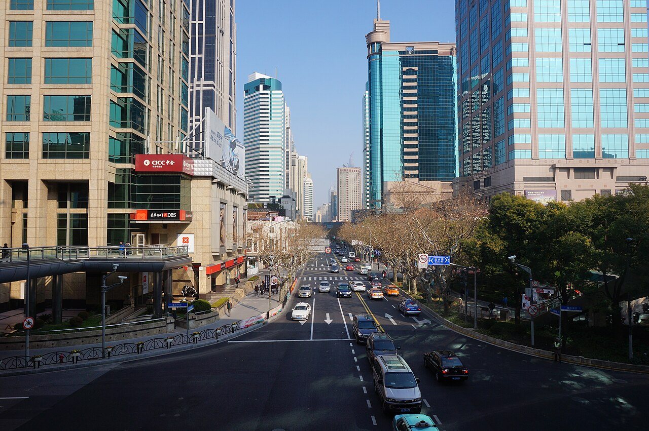 A cleaner elevated view down Middle Huaihai Road in Shanghai with traffic, towers, and a broad urban avenue.