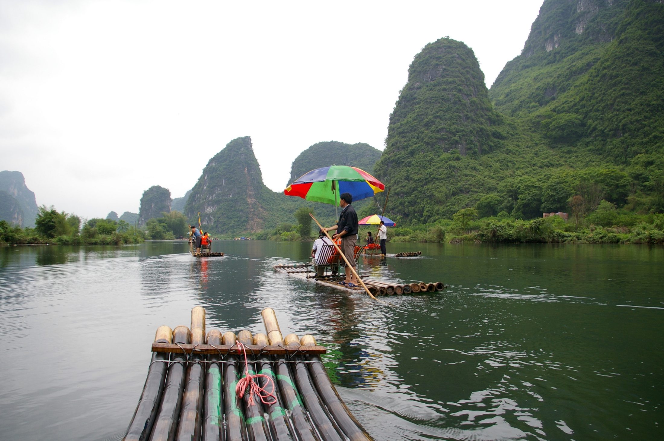 Bamboo rafts drifting along the Yulong River in Yangshuo with karst peaks rising behind them.