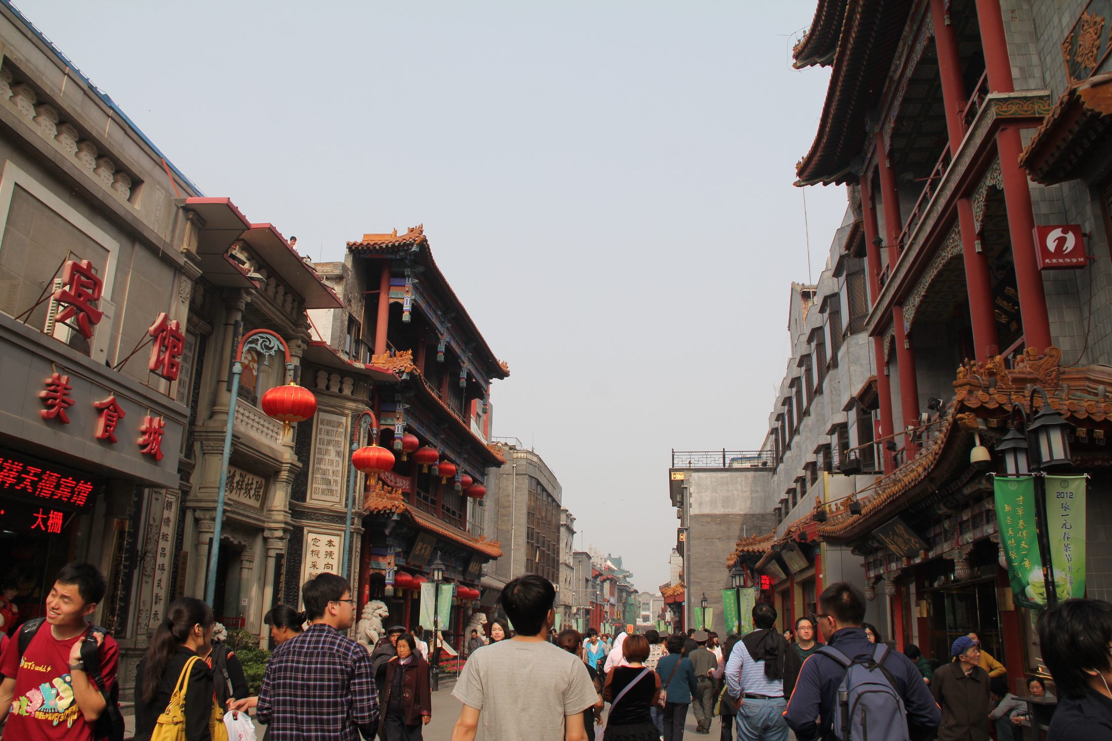 Pedestrians walking along Qianmen Street between traditional shopfronts in Beijing.