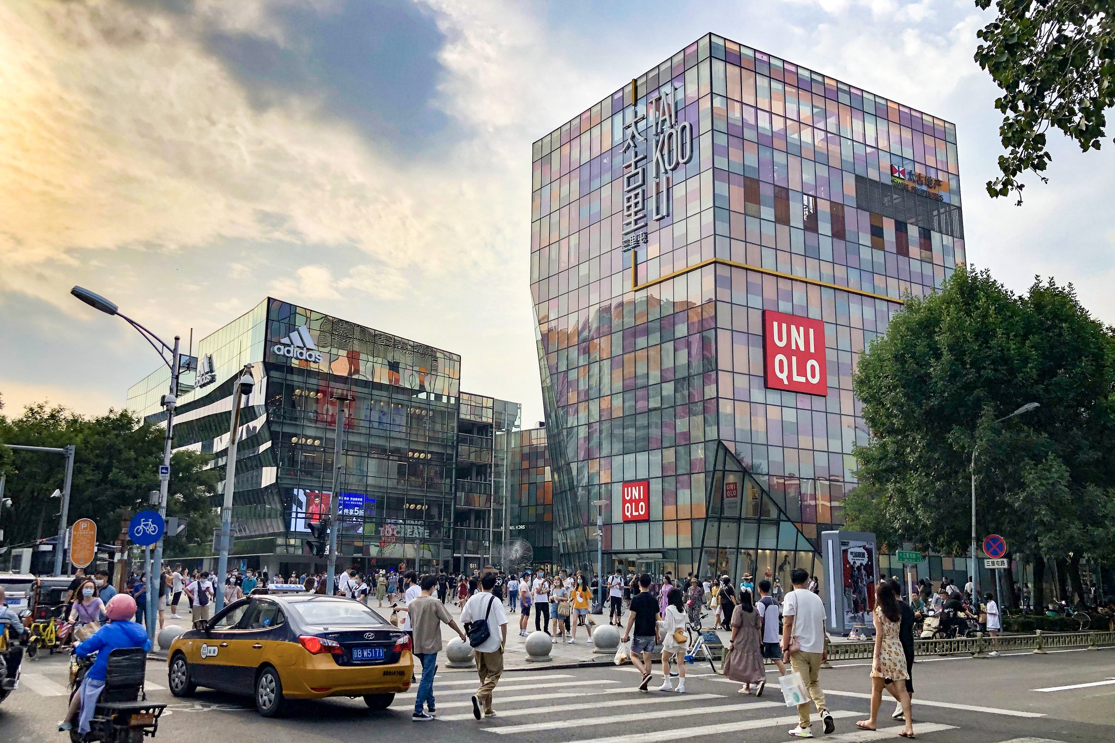 Crowds crossing in front of Taikoo Li Sanlitun's colorful glass storefronts in Beijing.