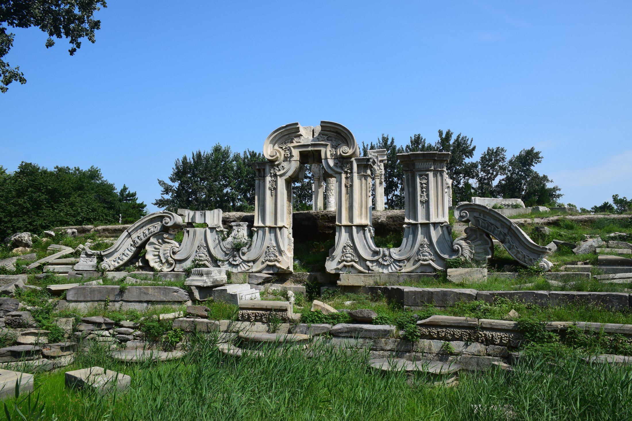 The stone Dashuifa ruins at Yuanmingyuan framed by summer greenery and open sky.