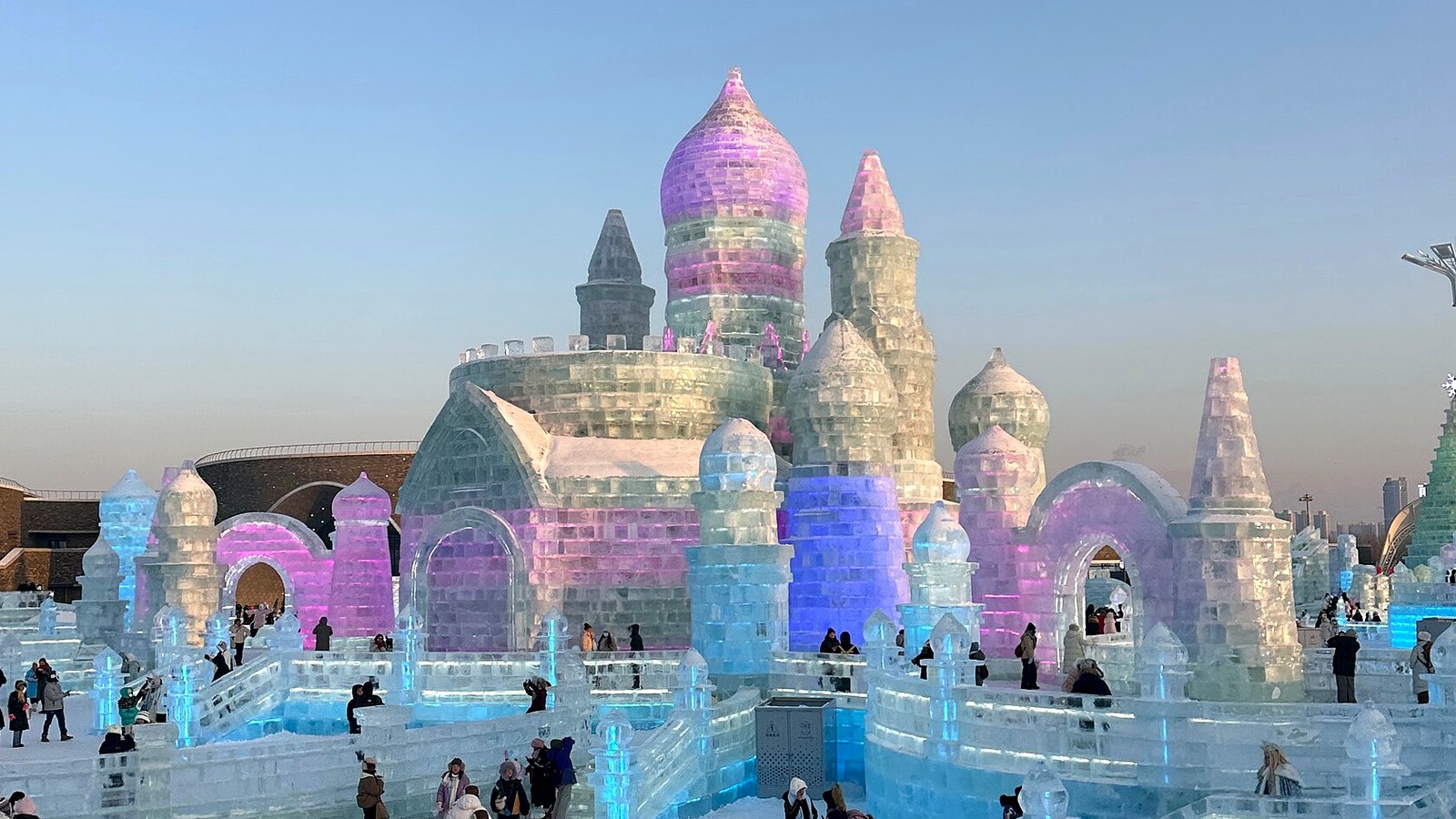 Pastel-lit ice replica of Saint Sophia Cathedral at Harbin Ice and Snow World under a bright winter sky.