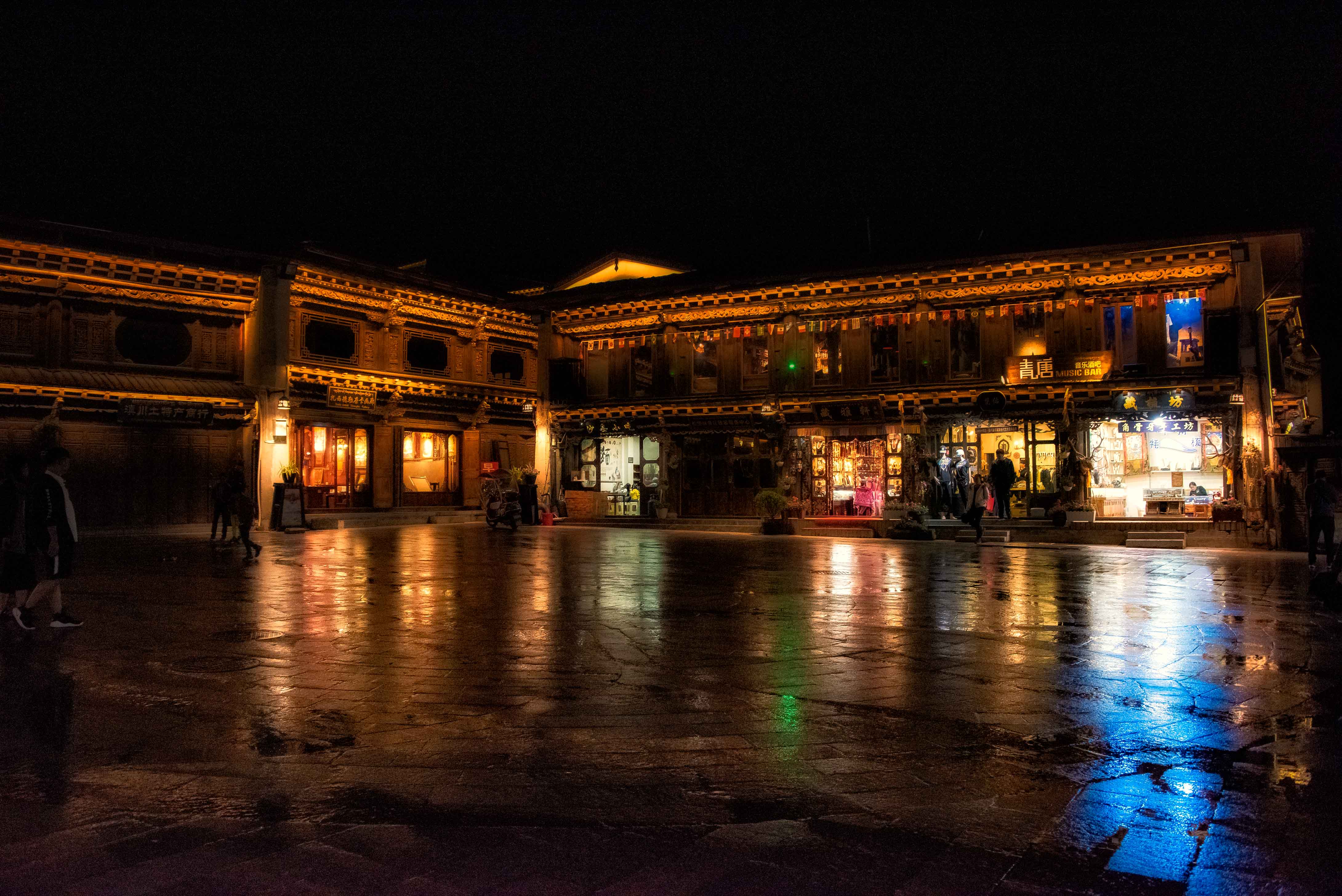 Dukezong Old Town in Shangri-La after rain, with warm wooden facades and reflections on the stone square at night.