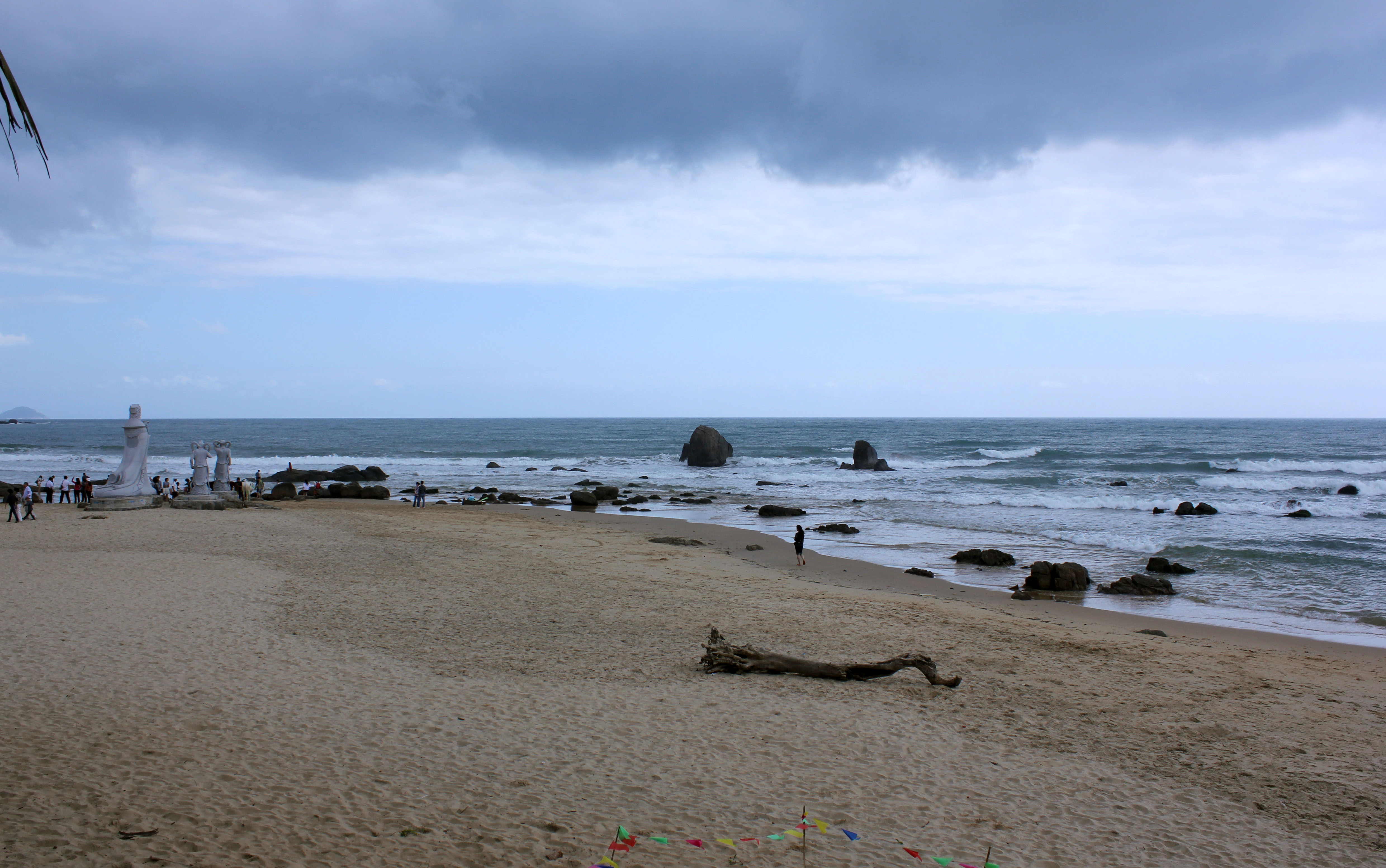 Riyue Bay in Wanning with a long crescent shoreline, layered green hills, and South China Sea surf under clear light.