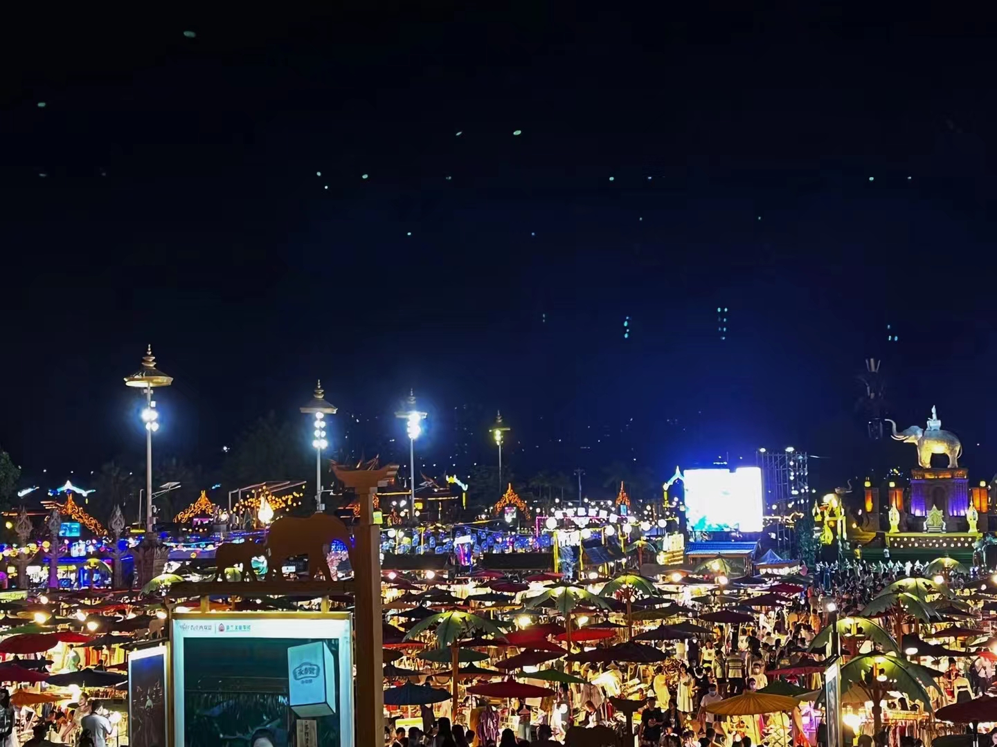 Mekong Starlight Night Market in Xishuangbanna with warm lantern light, temple silhouettes, and a dense tropical evening crowd.