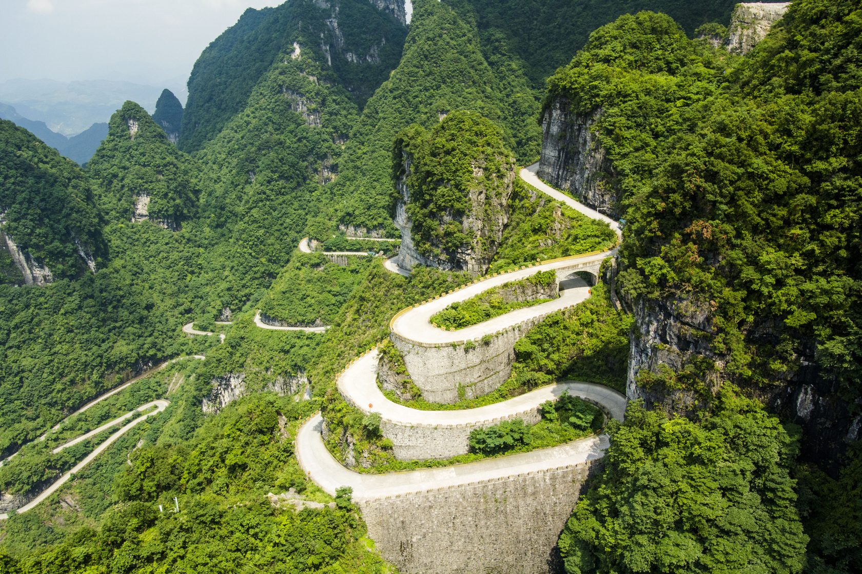 Winding mountain road on Tianmen Mountain in Zhangjiajie surrounded by vivid green cliffs.