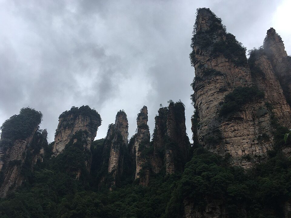 Towering sandstone pillars in Yuanjiajie under bright skies and deep green vegetation.